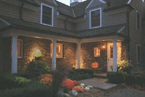 A porch at night with pumpkins on the steps and a warm light overhead.